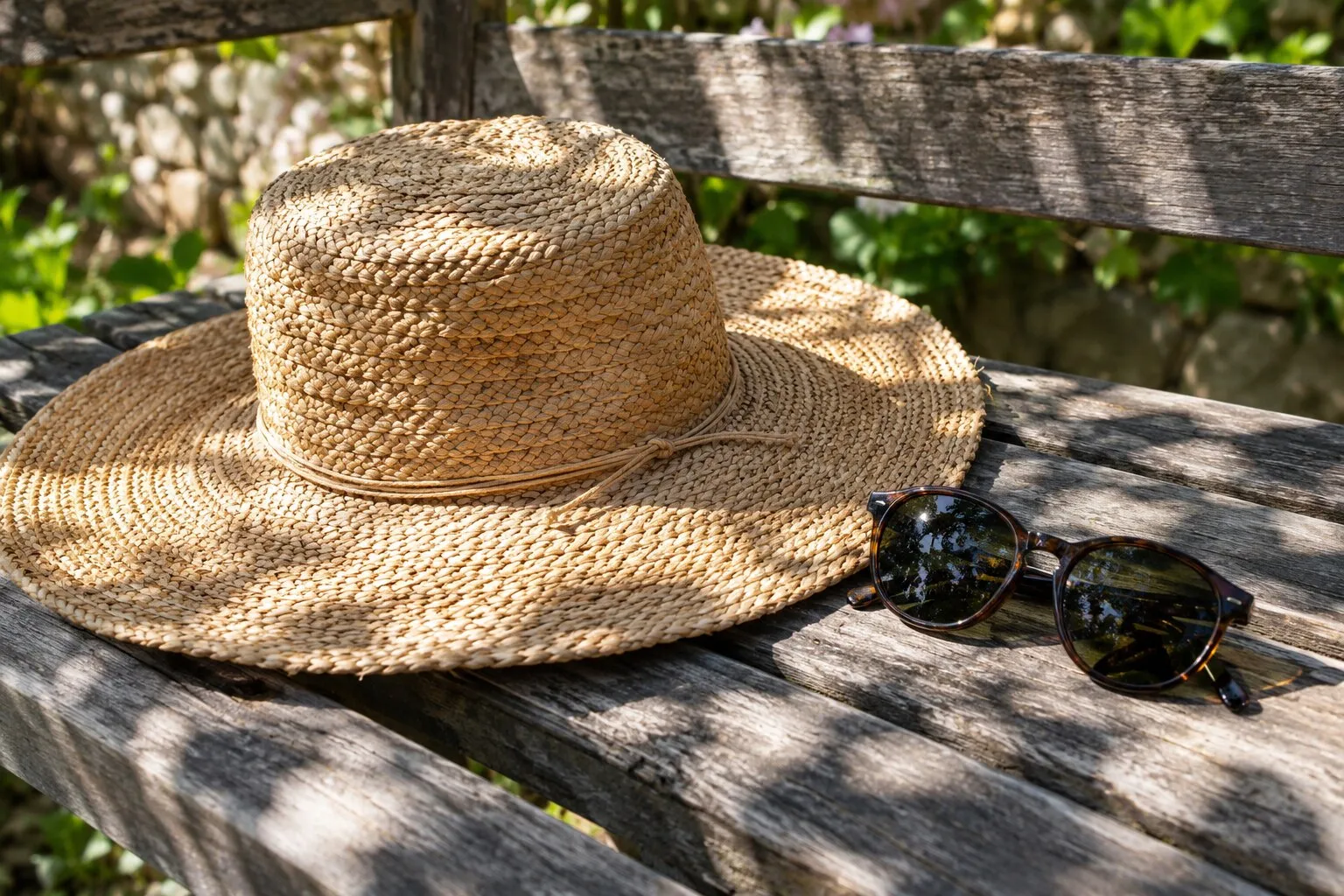 A straw sun hat and sunglasses on a garden bench in midday sun